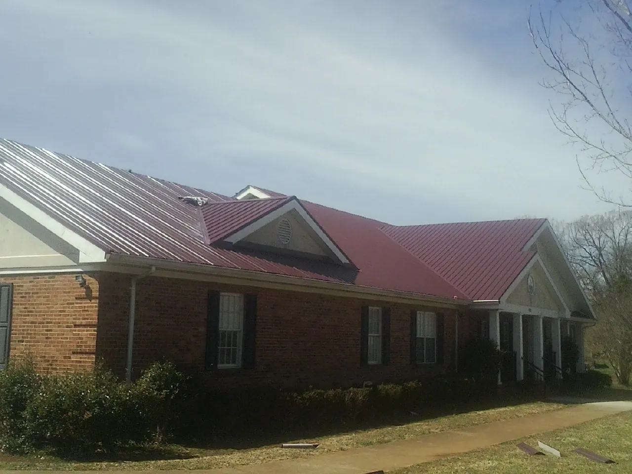 Red metal roof with gabled entries on a long brick building, from a Hail Damage Roof Repair job in Clio
