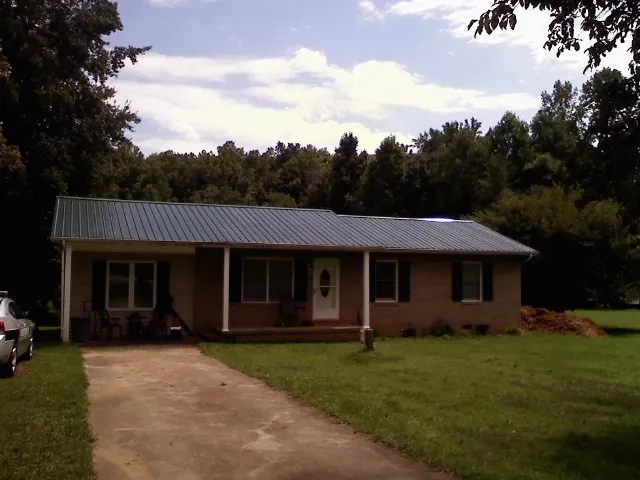 Dark green metal roof on a brick ranch with a covered porch in Clio